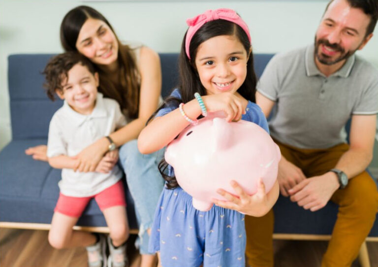 Zdjęcie przedstawiające siedzącą rodzinę, dziewczynka trzyma świnkę skarbonkę.